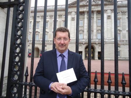 Photograph of Michael Mahoney outside Buckingham Palace Gates holding his Invitation from Queen Elizabeth II to attend the Queens garden party at Buckingham Palace.