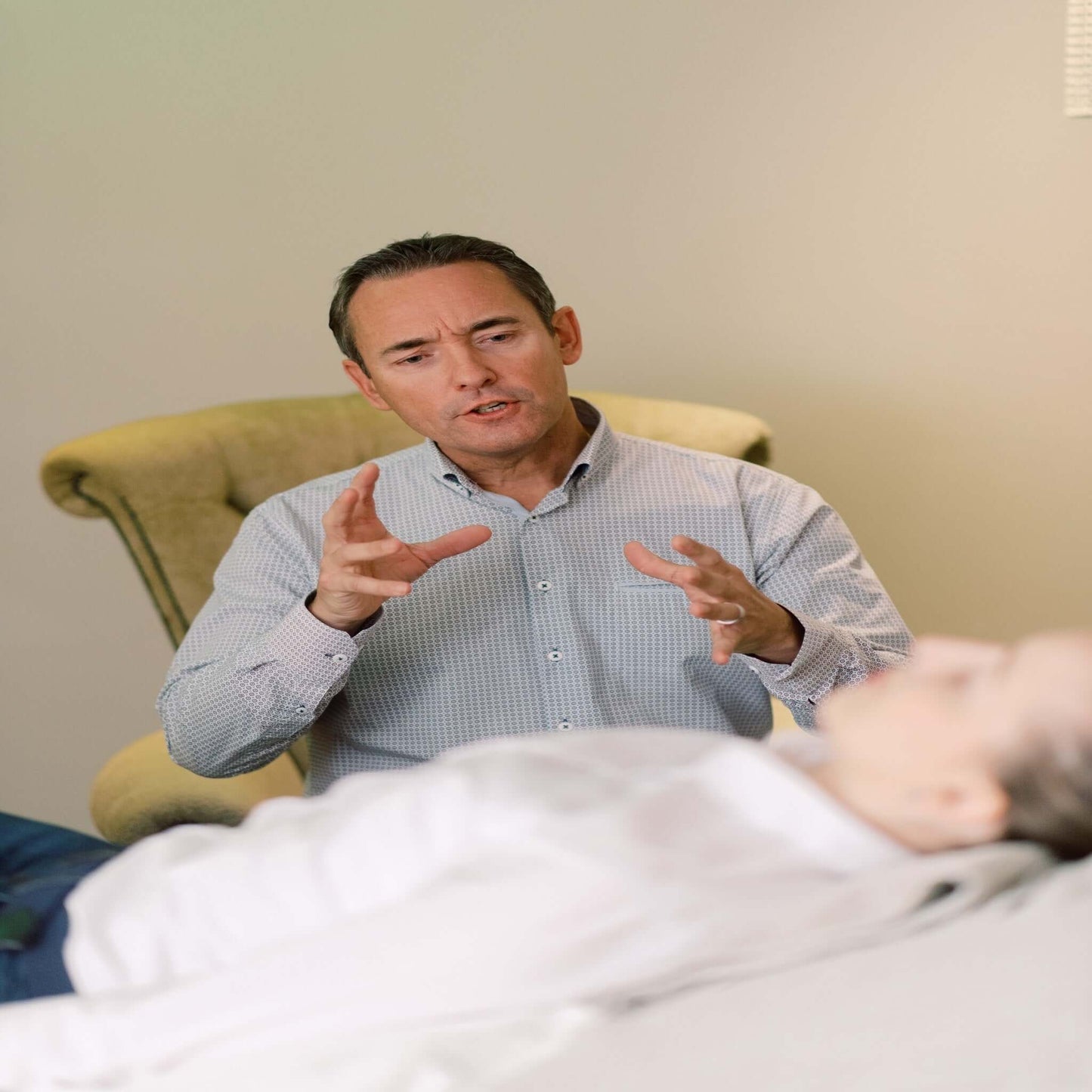 The image of a man speaking to a person lying down in a therapy session, implying the services of an IBS therapist register member